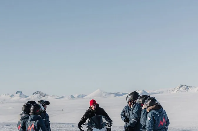 A group of riders in dark overalls and helmets standing together on a snowfield
